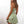 Vrouw in groene zomerjurk met madeliefjesprint, spaghetti bandjes, tegen witte achtergrond. Trendy damesmode, casual zomeroutfit.