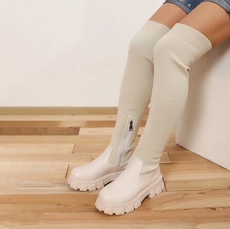 Witte kniehoge laarzen met dikke zolen en ritssluiting, gedragen door model op houten vloer. Trendy damesmode, comfortabele winterlaarzen.