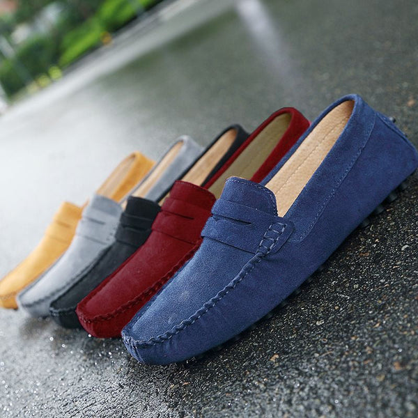 Verschillende kleuren suède loafers voor heren op natte straat, inclusief blauw, rood, zwart, grijs en geel. Stijlvolle casual schoenen.