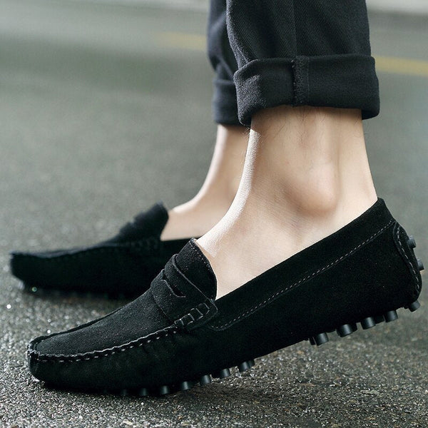 Zwarte suède loafers voor heren, gedragen op een natte straat. Comfortabele instappers met antislipzool, ideaal voor casual en formele gelegenheden.