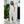 Vrouw in witte jumpsuit en sneakers poseert buiten bij groene planten en witte muur. Casual mode, zomerse outfit, comfortabele kledingstijl.