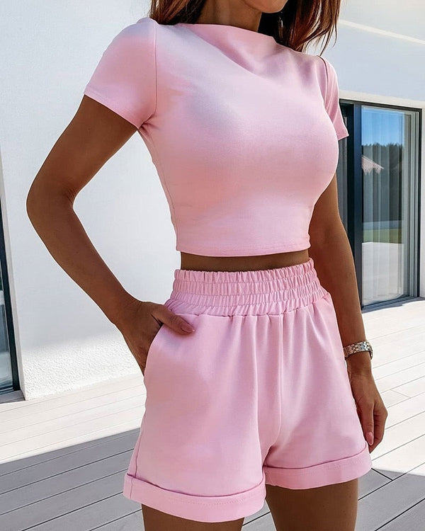 Vrouw in roze crop top en shorts, zomerse outfit, casual mode, buiten op terras, trendy dameskleding, comfortabele stijl, zonnige dag.
