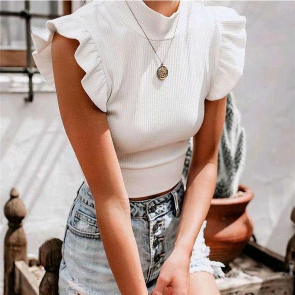 Vrouw in witte geribbelde top met ruches en spijkerbroek, draagt een ketting. Zomerse mode, casual outfit, trendy kledingstijl.