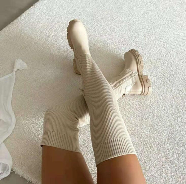 Beige, ribgebreide kniehoge laarzen met dikke zolen op een witte tapijtachtergrond. Modieuze dameslaarzen, trendy herfst- en winterstijl.