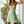Vrouw in groene zomerjurk met bloemenprint, staand op veranda. Trendy damesmode, casual zomeroutfit, perfecte keuze voor warme dagen.