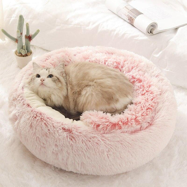 Kat ligt comfortabel in roze, pluche kattenmand op wit beddengoed; luxe huisdierbed, zachte kattenmand, huisdiercomfort, gezellige kattenmand.