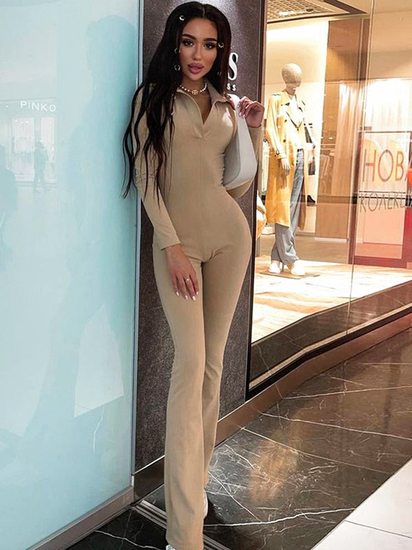 Vrouw in beige jumpsuit poseert in moderne winkelcentrum, stijlvolle mode, lange mouwen, trendy outfit, winkelachtergrond, casual chic look.