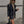 Vrouw in zwarte leren blazer en beige coltrui, draagt zonnebril en zwarte tas, loopt buiten op trottoir. Modieuze herfstoutfit, stedelijke stijl.