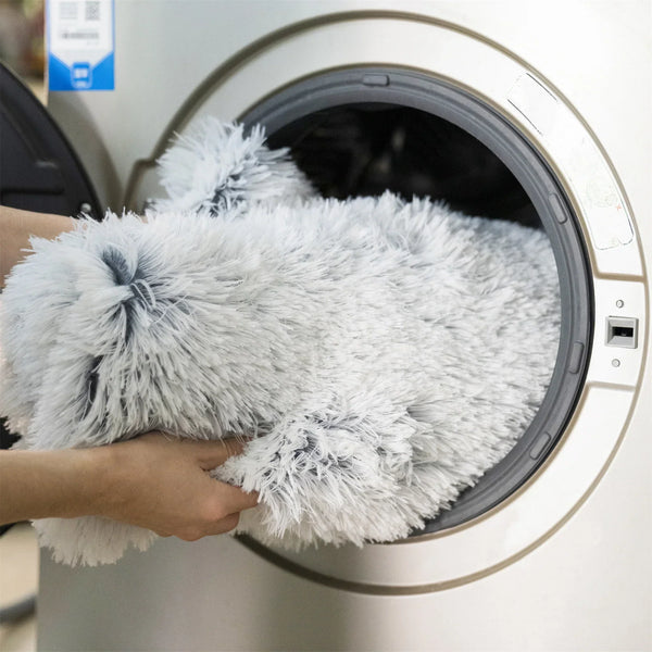 Handen plaatsen een grijs, pluchen hondenspeelgoed in een wasmachine. Zacht speelgoed wassen, hygiëne, huisdierverzorging.