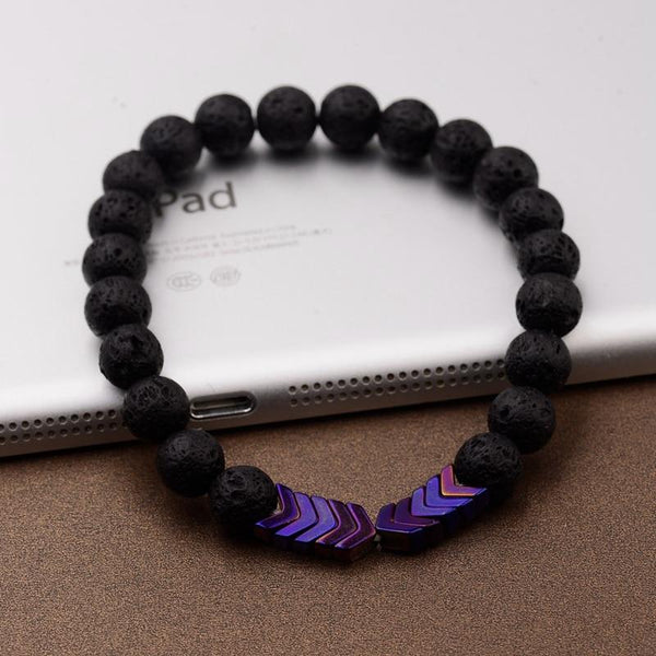 Zwart lavasteen armband met paarse pijlvormige kralen, stijlvol en modern, liggend op een bruine ondergrond naast een tablet.