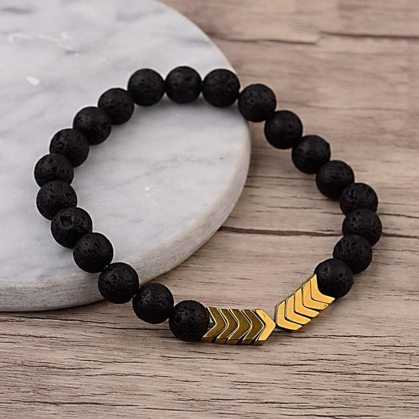 Zwarte lavasteen armband met gouden pijlvormige accenten op houten achtergrond, stijlvolle sieradenaccessoire voor mannen en vrouwen.