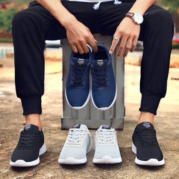Man toont drie paar sportieve sneakers in blauw, grijs en zwart. Comfortabele hardloopschoenen voor heren, casual en stijlvol design.