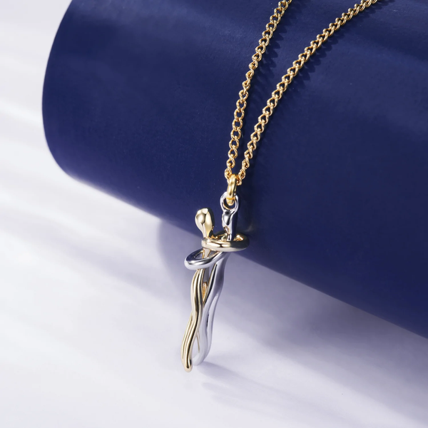 Gouden en zilveren hanger met omhelzend paar ontwerp aan een ketting, elegant sieraad op blauwe achtergrond, perfect voor romantische gelegenheden.