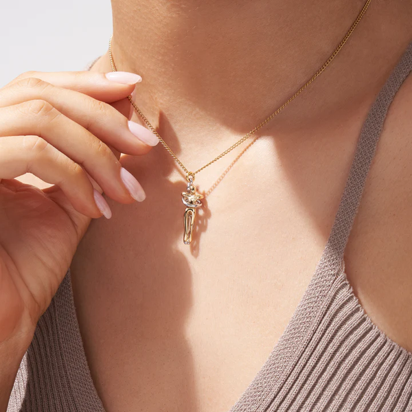 Gouden ketting met elegante hanger, gedragen door vrouw in beige top. Stijlvolle sieraden, modieuze accessoires, close-up.