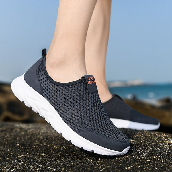Donkergrijze ademende sneakers voor heren op rotsachtige ondergrond, ideaal voor wandelen en hardlopen. Comfortabele sportschoenen met witte zool.