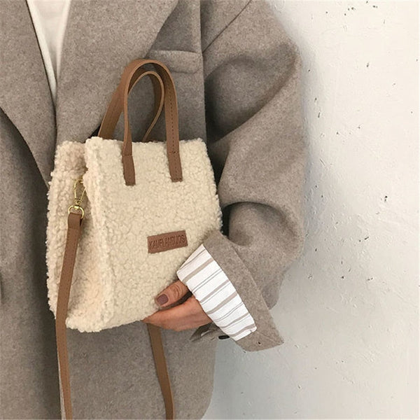 Vrouw met beige teddy schoudertas en bruine leren handvatten, gekleed in grijze jas. Modieuze winteraccessoires, trendy damesmode.
