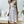 Vrouw in witte jurk met zwarte stippen en strikceintuur, staand in moderne woonkamer. Trendy zomerjurk, elegante mode, casual chique stijl.