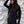 Vrouw in zwarte jumpsuit voor witte keramische achtergrond, modieuze outfit, lange mouwen, trendy stijl, zwarte tas, casual chique look.