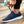 Donkerblauwe sportschoen met witte zool, gedragen door een persoon die de veters strikt. Perfect voor hardlopen en casual gebruik. Comfortabel en stijlvol.