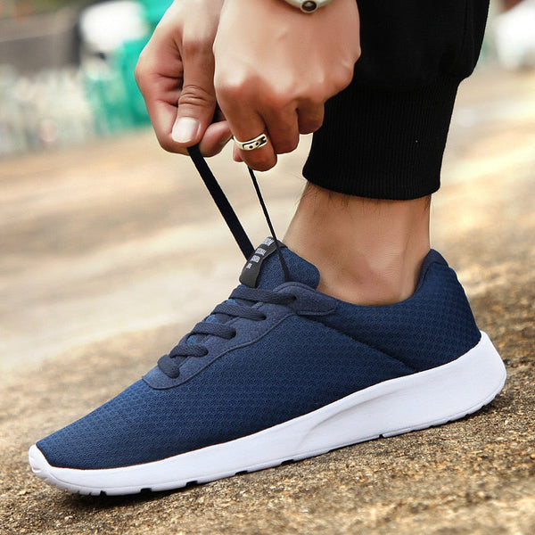 Donkerblauwe sportschoen met witte zool, gedragen door een persoon die de veters strikt. Perfect voor hardlopen en casual gebruik. Comfortabel en stijlvol.