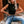 Vrouw in zwarte mouwloze top en gescheurde jeans, zittend buiten. Modieuze casual outfit, zonnebril, gouden ketting. Trendy dameskleding.