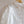 Witte kanten blouse met parelknopen, elegante vintage stijl, gedetailleerd bloemenpatroon, hangend aan houten hanger tegen witte achtergrond.