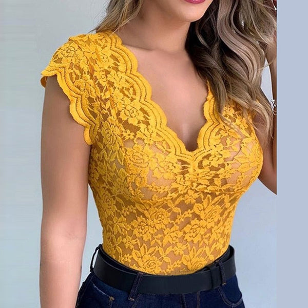 Vrouw in gele kanten top met diepe V-hals, korte mouwen en bloemenpatroon, gecombineerd met een zwarte riem en donkerblauwe jeans.