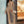 Vrouw in beige jumpsuit poseert voor winkel, draagt witte sneakers en schoudertas. Modieuze outfit, casual stijl, winkelcentrum achtergrond.