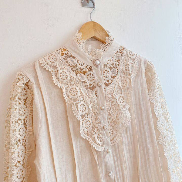 Vintage ivoorkleurige blouse met kanten details en parelknopen, hangend aan houten hanger. Elegante damesmode, romantische stijl, boho chic.