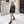 Vrouw in zwarte leren blazer en rok, draagt designer schoudertas en laarzen, loopt langs stenen gebouw. Mode, straatstijl, herfstkleding.