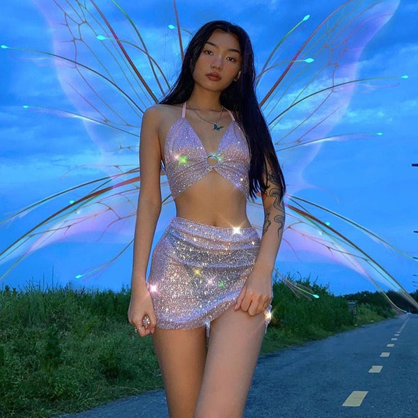Jonge vrouw in glinsterende feeënjurk met vleugels, poseert op een landweg bij zonsondergang. Magische sfeer, fantasie, cosplay, feeënmode.