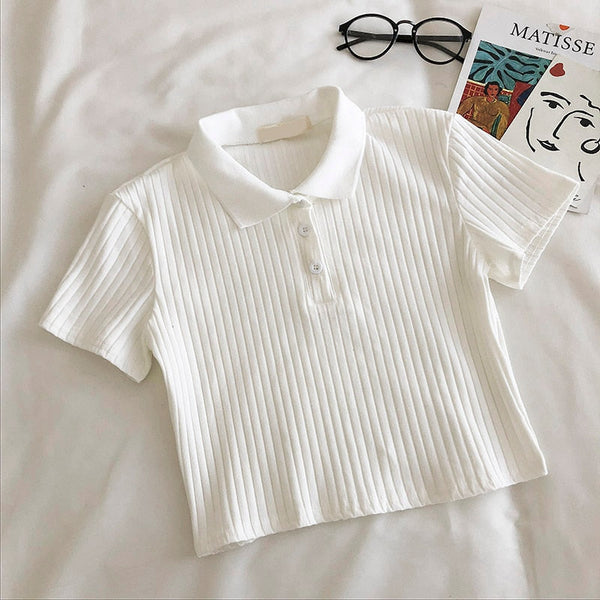 Witte geribbelde polo crop top op bed met bril en Matisse boek. Trendy dameskleding, casual stijl, zomeroutfit, modieuze top.