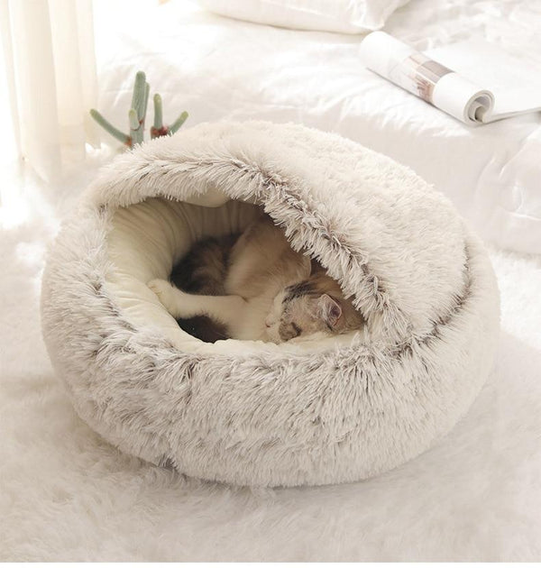 Kat slaapt in een ronde, pluche kattenmand op een witte vloer. Comfortabele huisdierbedden, zachte kattenmand, huisdieraccessoires.