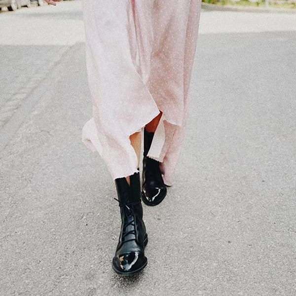 Vrouw in roze jurk met zwarte leren laarzen loopt op stoep. Modieuze dameskleding, trendy schoenen, straatmode.