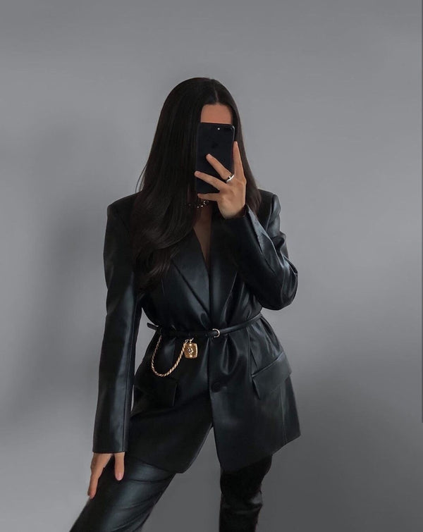 Vrouw in zwarte leren blazer met gouden kettingriem, maakt selfie. Modieuze outfit, trendy leren kleding, stijlvolle damesmode.