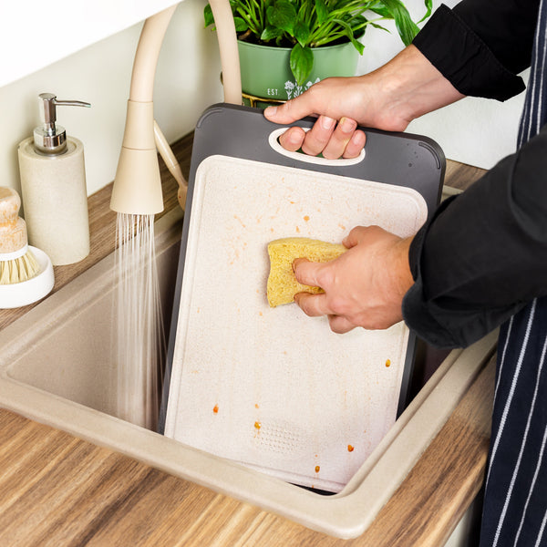 Handen wassen snijplank in gootsteen met spons en stromend water, keukenaccessoires, duurzaam schoonmaken, keukenhygiëne.