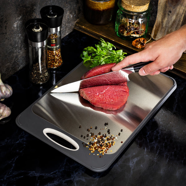 Hand snijdt rauw rundvlees op metalen snijplank met mes, omringd door kruiden en specerijen. Keukenvoorbereiding, koken, vlees snijden.