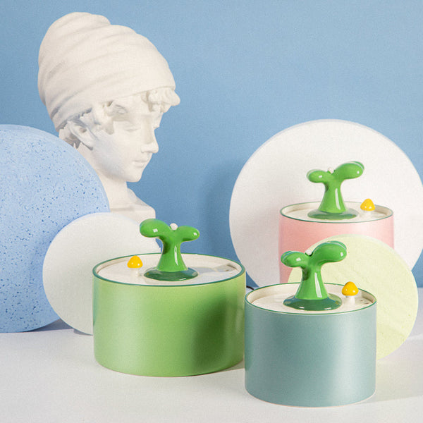 Drie kleurrijke, moderne luchtbevochtigers met groene tuitjes voor een buste van een klassieke sculptuur, tegen een pastelblauwe achtergrond.