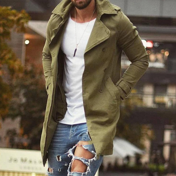 Man in groene lange jas, witte T-shirt en gescheurde jeans. Stijlvolle herenkleding, herfstmode, stedelijke achtergrond.