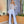 Vrouw in elegante lichtblauwe jumpsuit met verenaccenten, staand in moderne interieursetting met planten. Perfect voor modieuze avondkleding.