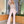 Vrouw in elegante roze jumpsuit met veren en glinsterende details, staand in moderne interieursetting met planten en houten elementen.