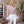 Vrouw in elegante witte jumpsuit met veren en glinsterende top, staand voor een stenen gebouw. Perfect voor chique evenementen en modieuze gelegenheden.