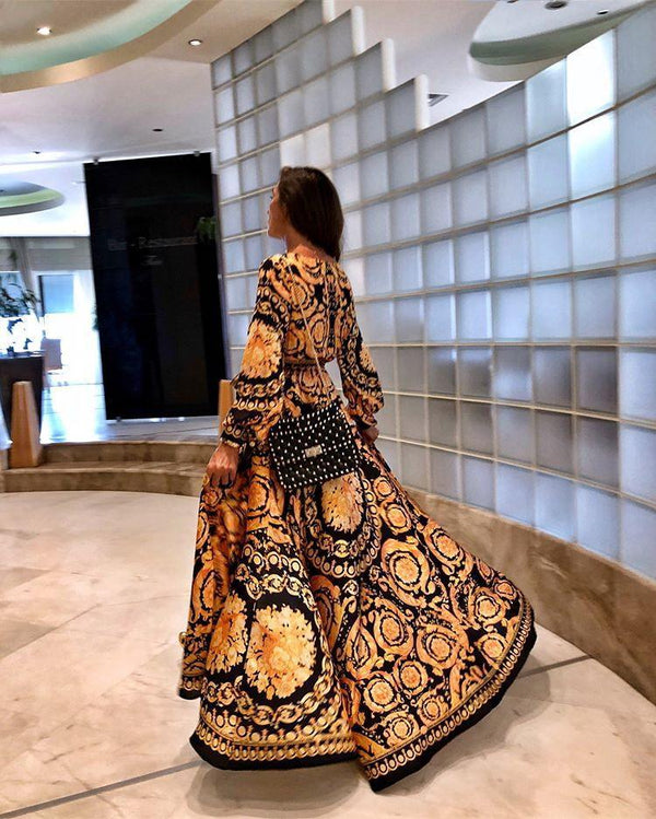 Vrouw in kleurrijke, lange jurk met barokprint loopt door modern interieur. Stijlvolle mode, elegante outfit, trendy design, luxe uitstraling.
