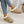 Vrouwelijke voeten in beige suède pantoffels met witte voering, gedragen met gescheurde jeans. Comfortabele damesmode, casual schoeisel.