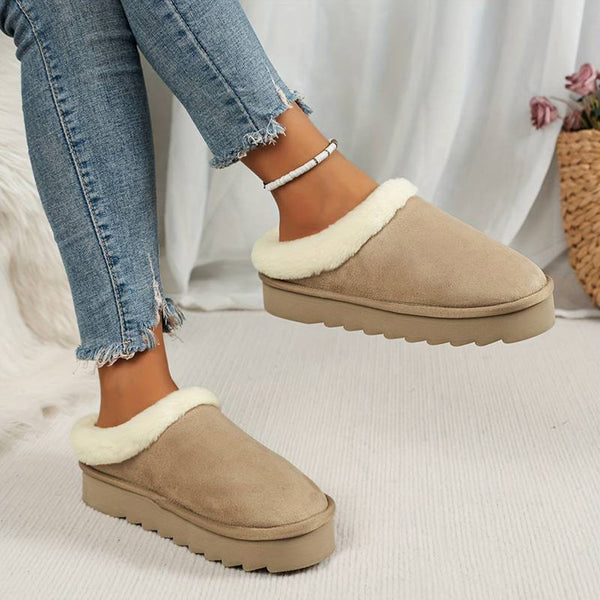 Vrouwelijke voeten in beige suède pantoffels met witte voering, gedragen met gescheurde jeans. Comfortabele damesmode, casual schoeisel.