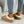 Vrouw draagt beige pantoffels met witte voering en dikke zool, gecombineerd met blauwe jeans. Comfortabele wintermode, casual stijl.