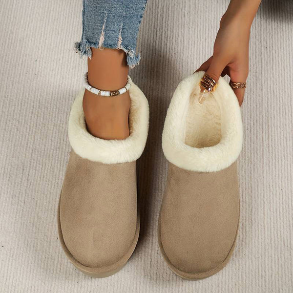 Vrouw draagt beige pantoffels met witte bontvoering, gecombineerd met gescheurde jeans. Comfortabele wintermode, warme damespantoffels.