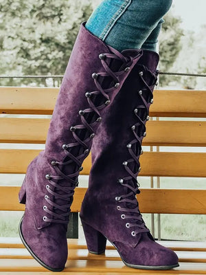 Paarse suède laarzen met hoge hak en veters, gedragen door persoon op houten bank. Modieuze dameslaarzen, trendy herfst- en winterstijl.