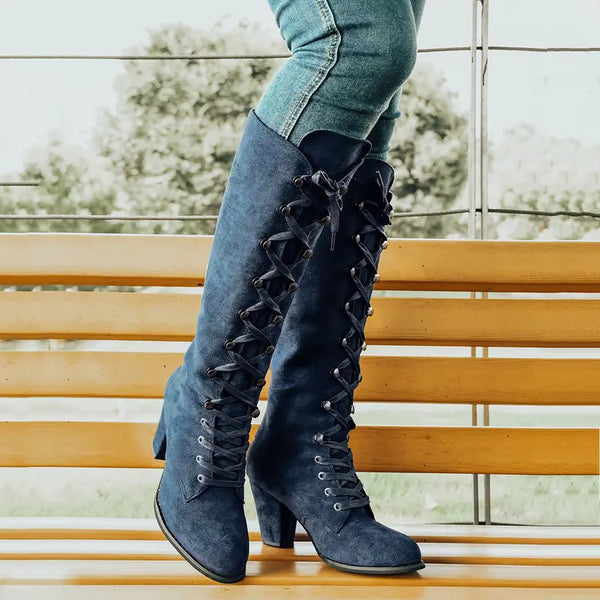 Blauwe suède veterlaarzen met hoge hakken, gedragen door een persoon in jeans, zittend op een houten bank. Stijlvolle dameslaarzen voor herfstmode.