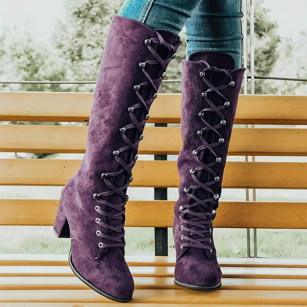 Paarse suède laarzen met veters, gedragen door persoon op houten bank. Trendy damesmode, hoge hakken, herfst/winter stijl.